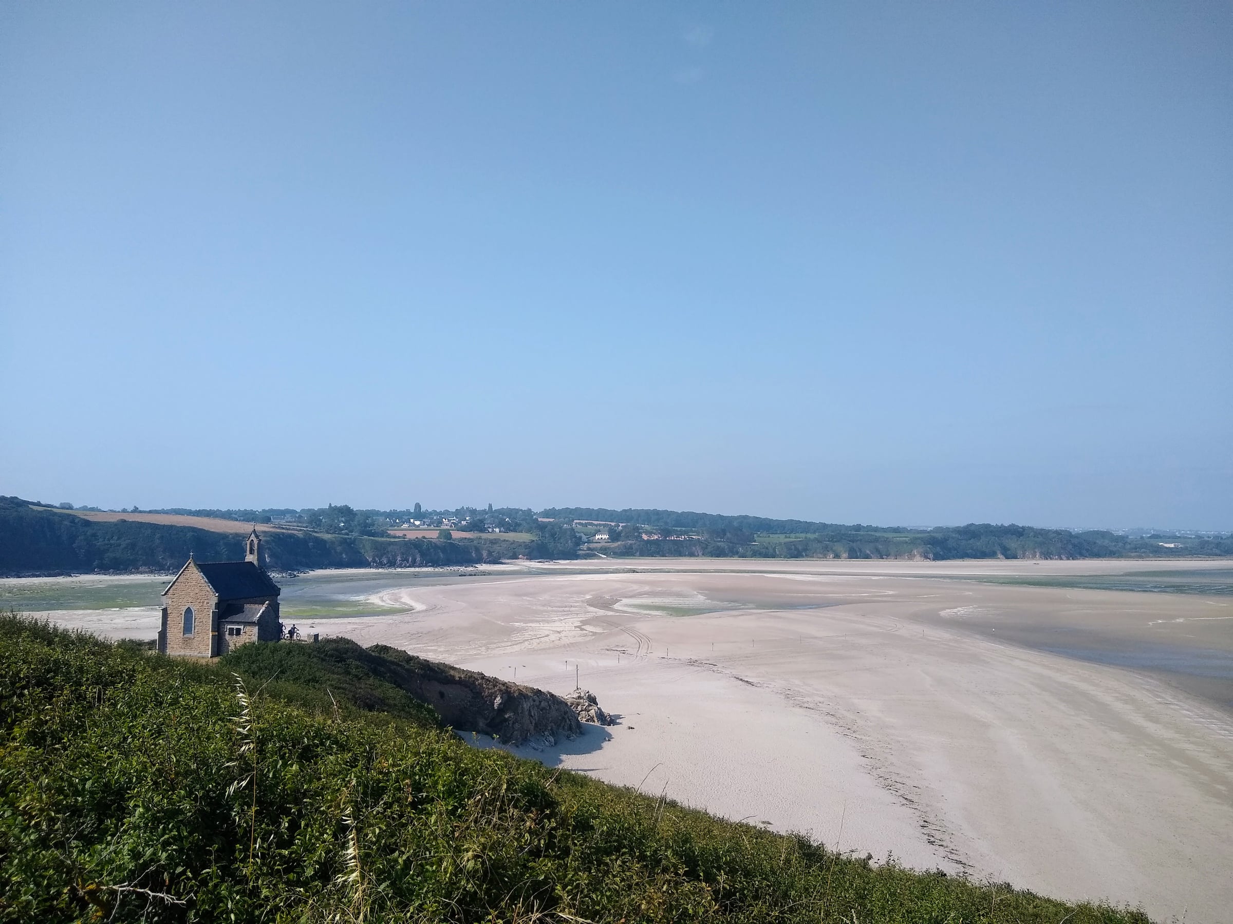 Petite chapelle de pierre sur la côte, devant une vaste étendue de sable à marée basse.