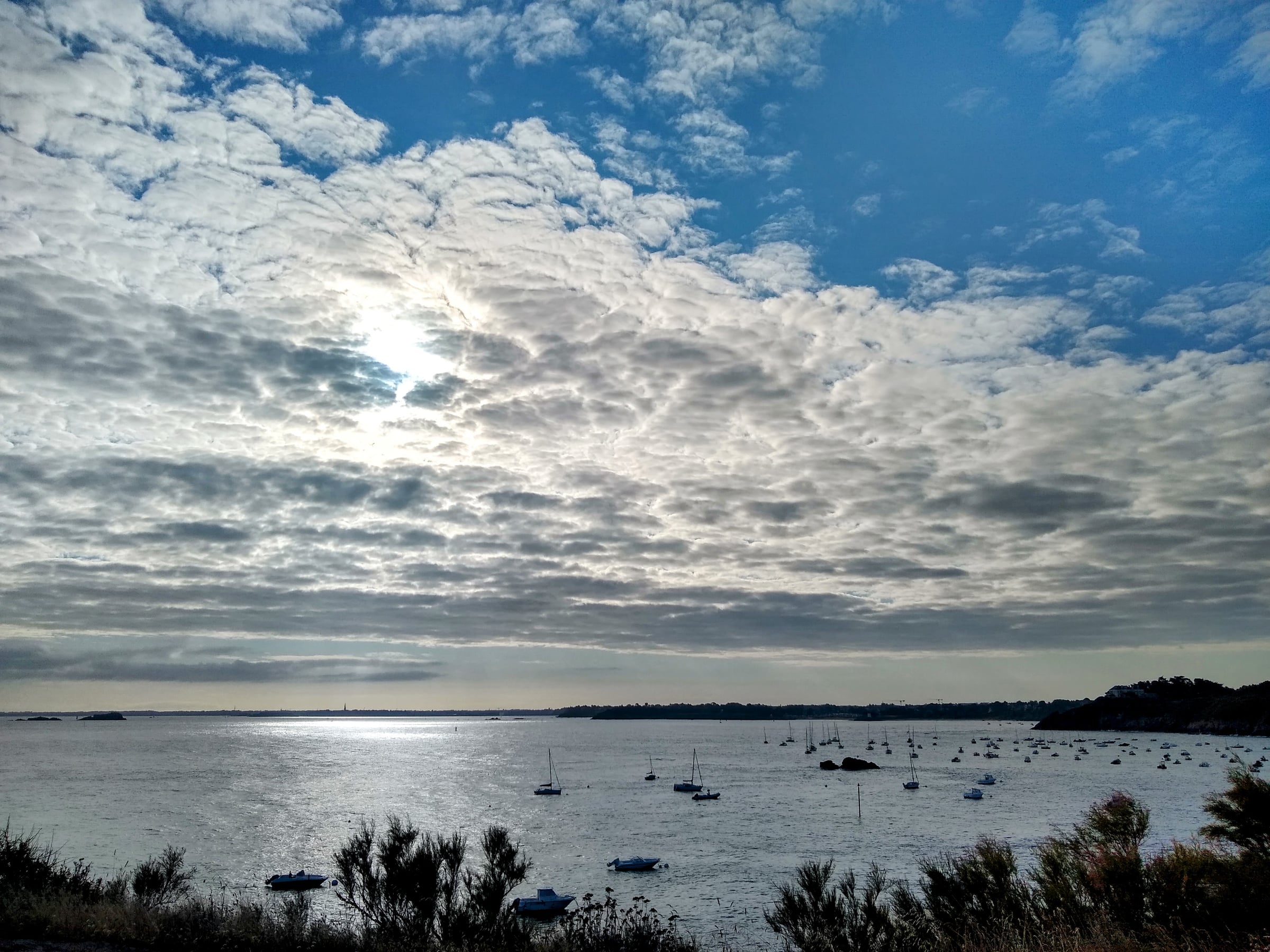 Bateaux au mouillage dans une baie, avec le soleil qui filtre à travers les nuages.