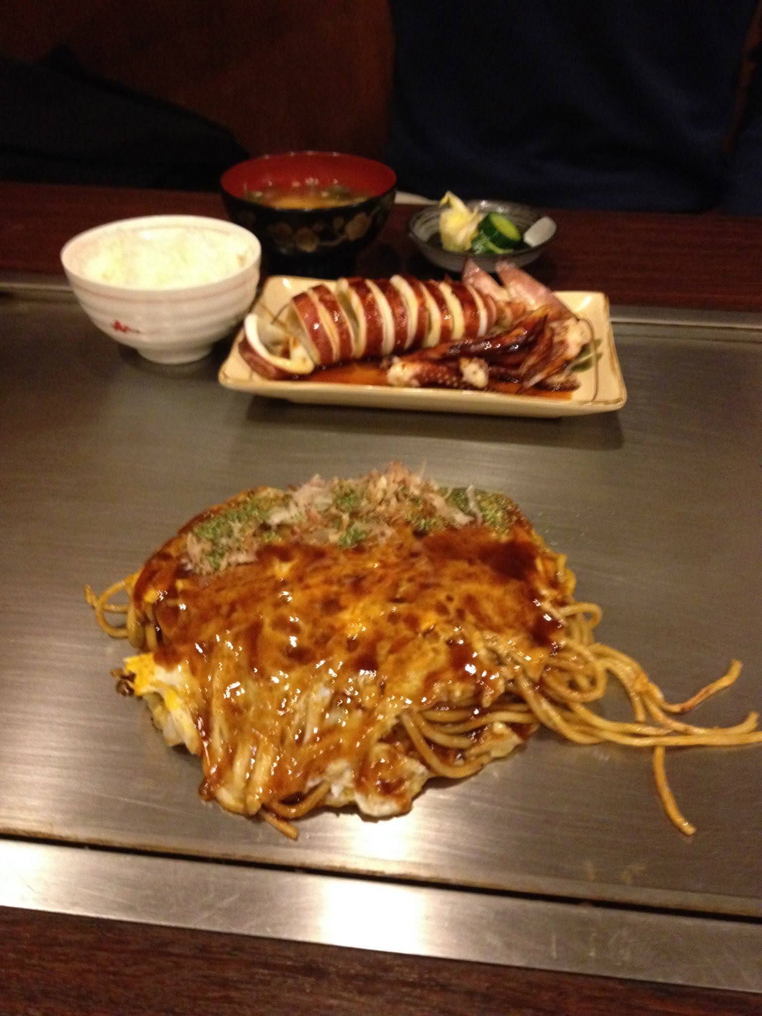 Deux plats de cuisine japonaise sur une plaque de cuisson, avec du riz et de petits bols au fond.