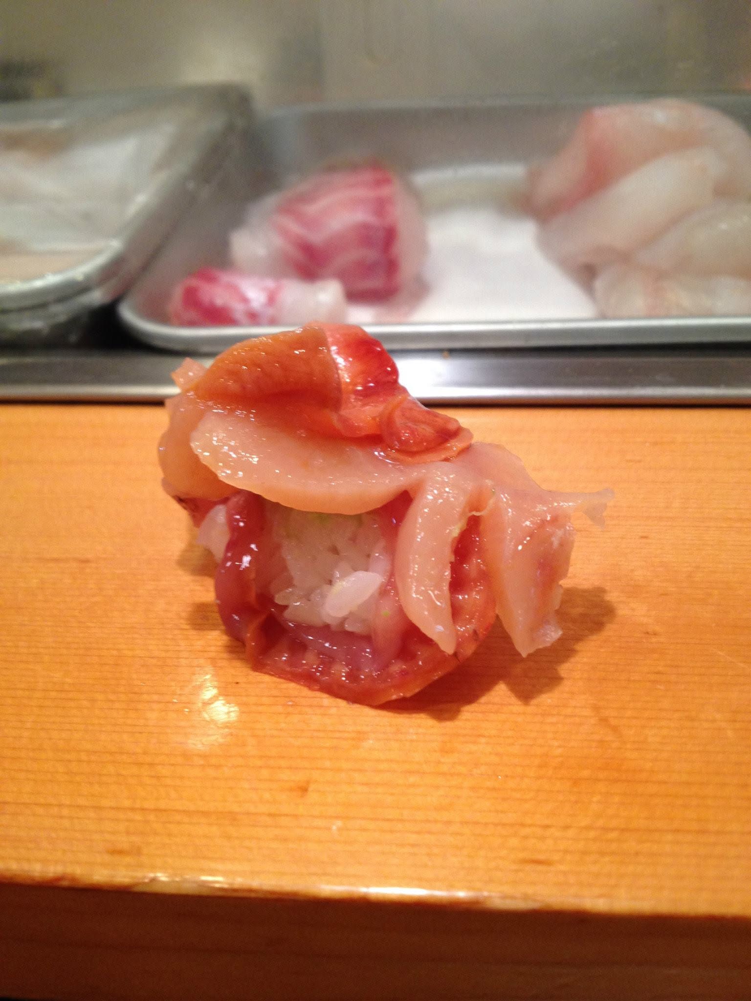 Sushi de poisson rose sur un comptoir en bois, devant une vitrine de poissons.