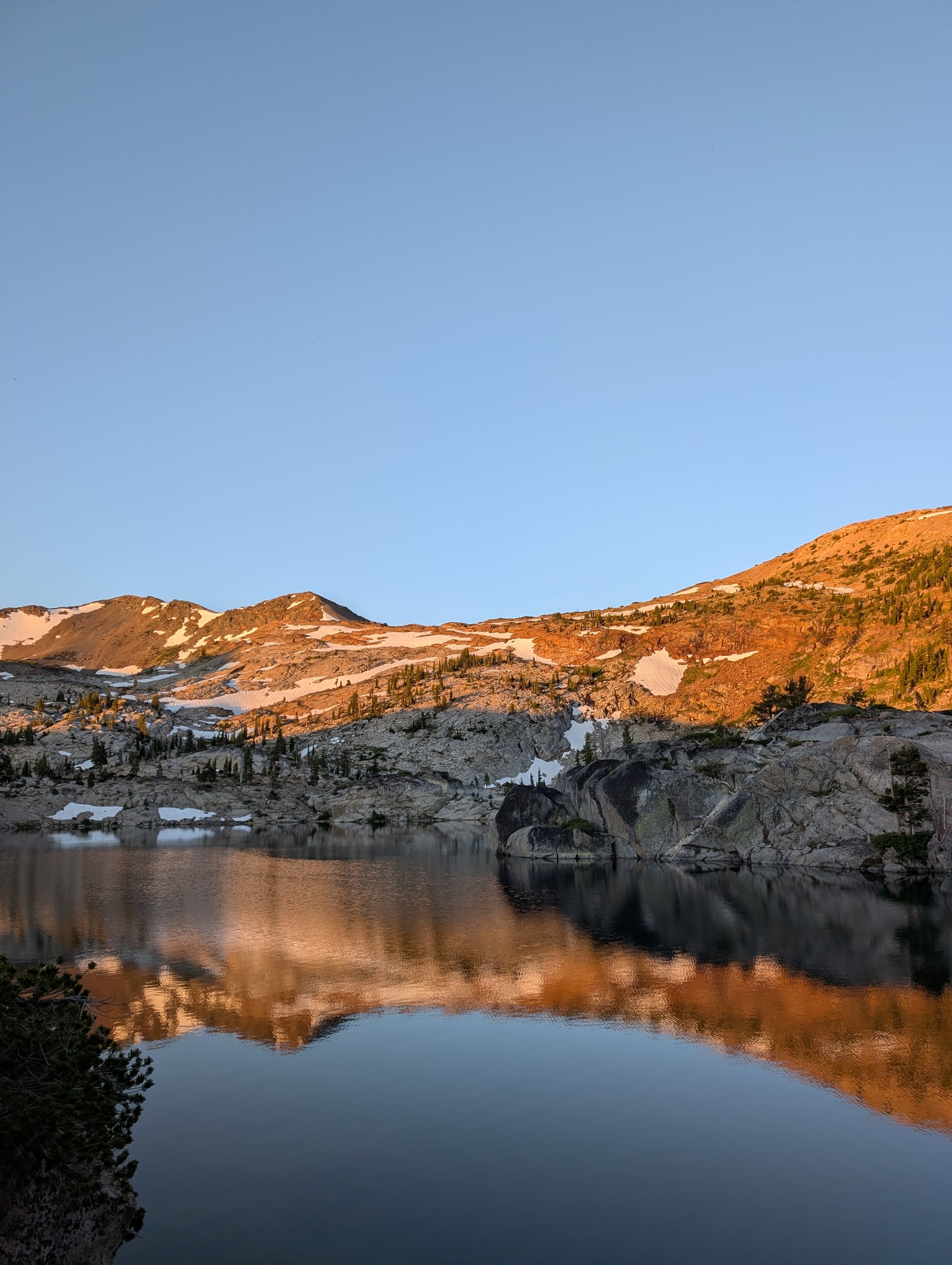 Lac reflétant des rochers et des crêtes éclairées d’une lumière dorée.