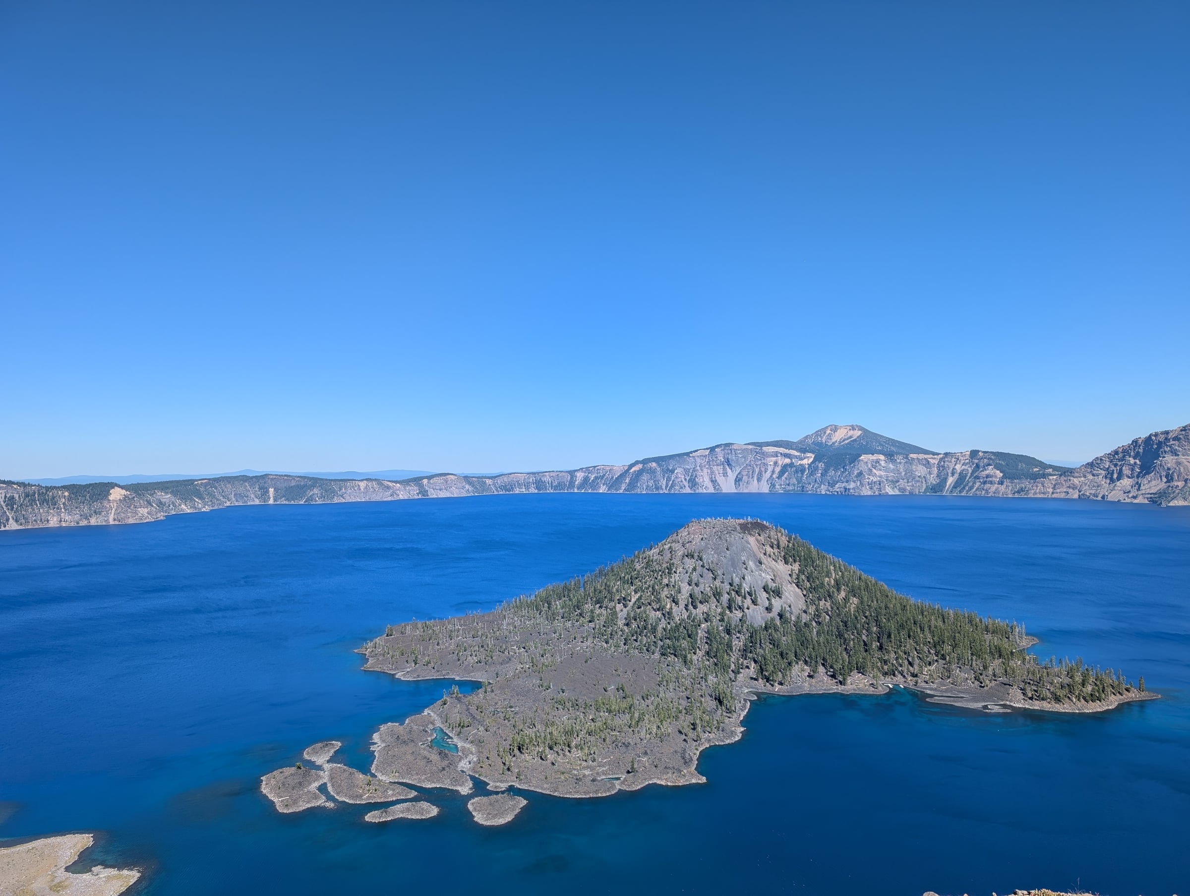 Île volcanique boisée dans un grand lac d’un bleu intense, entouré de falaises.