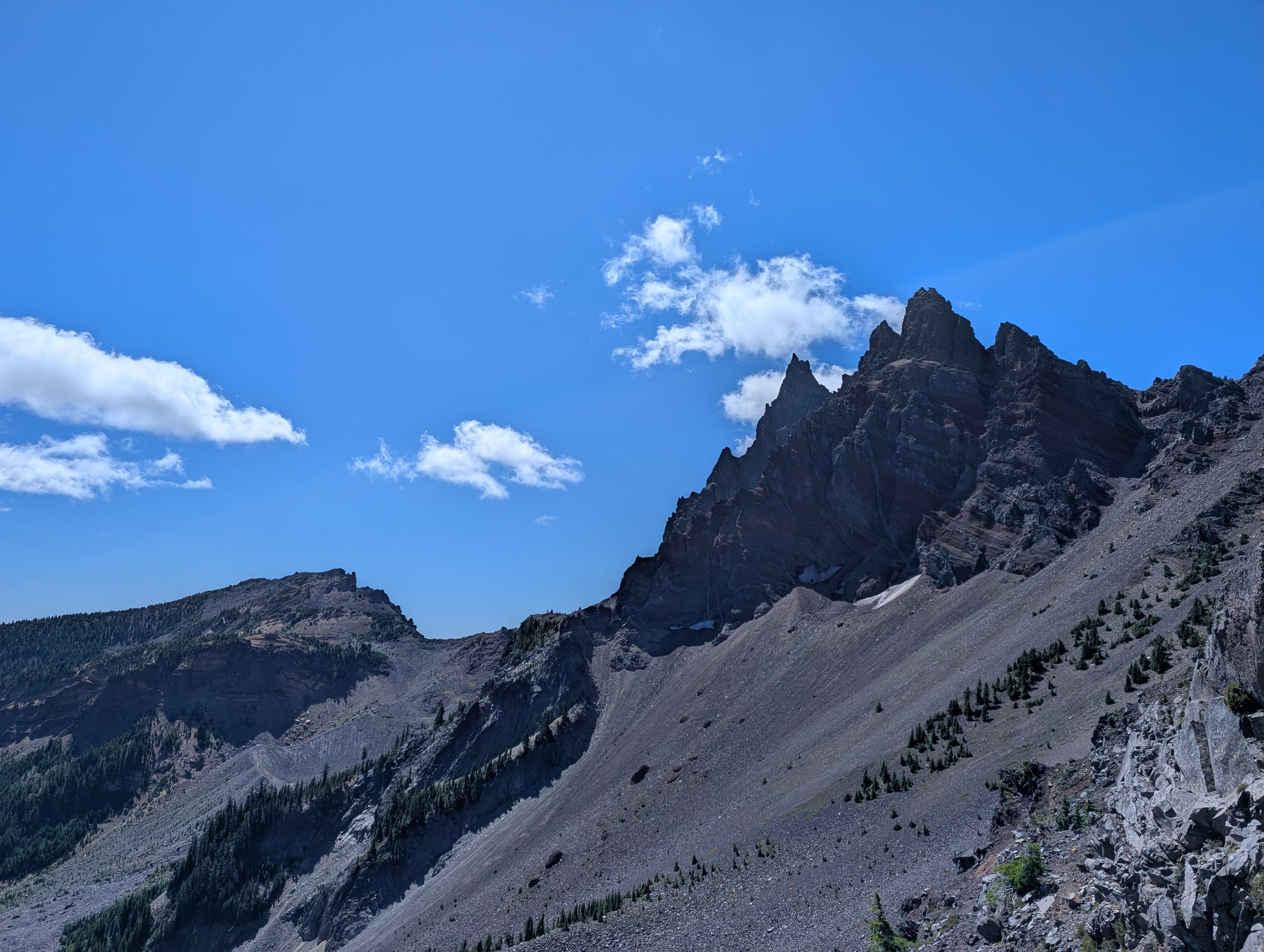 Aiguilles et pentes rocheuses avec quelques pins sous un ciel bleu parsemé de nuages.