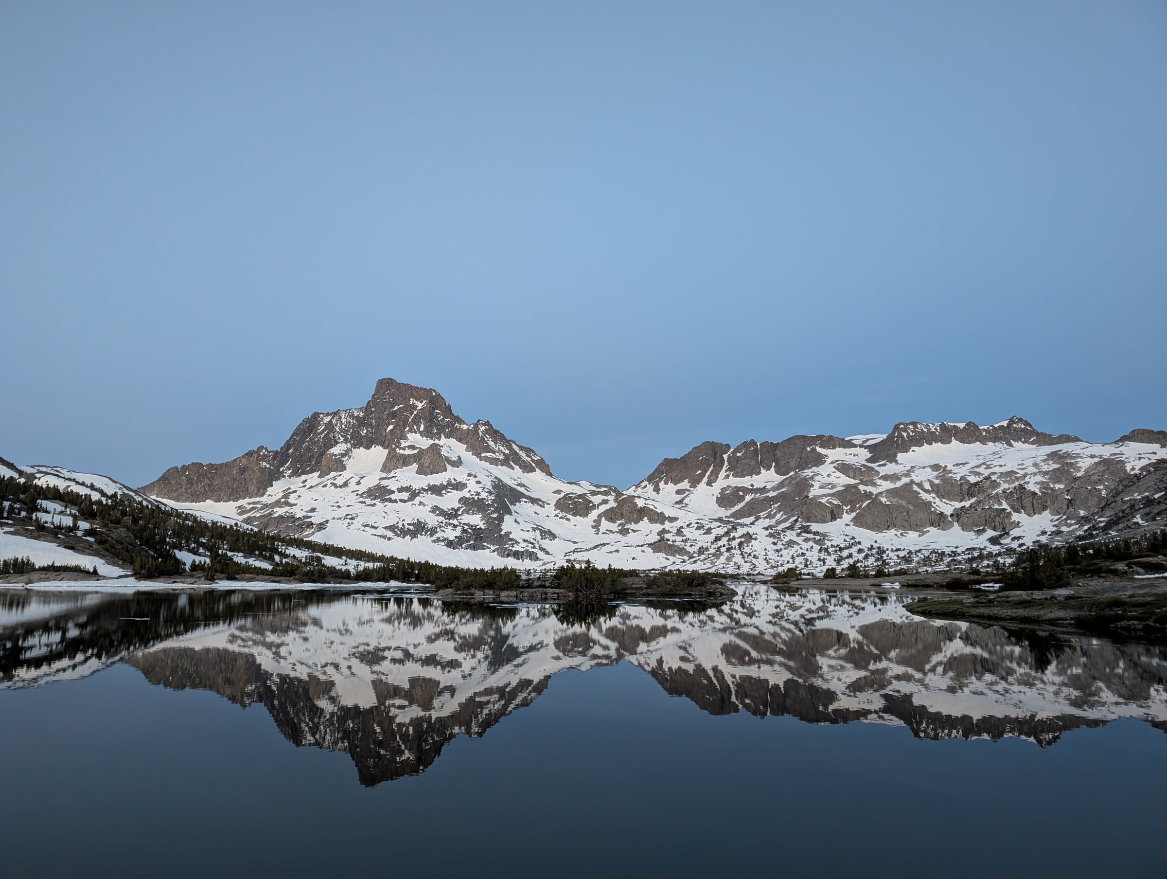 Sommets enneigés et îlots de pins reflétés dans l’eau calme d’un lac.