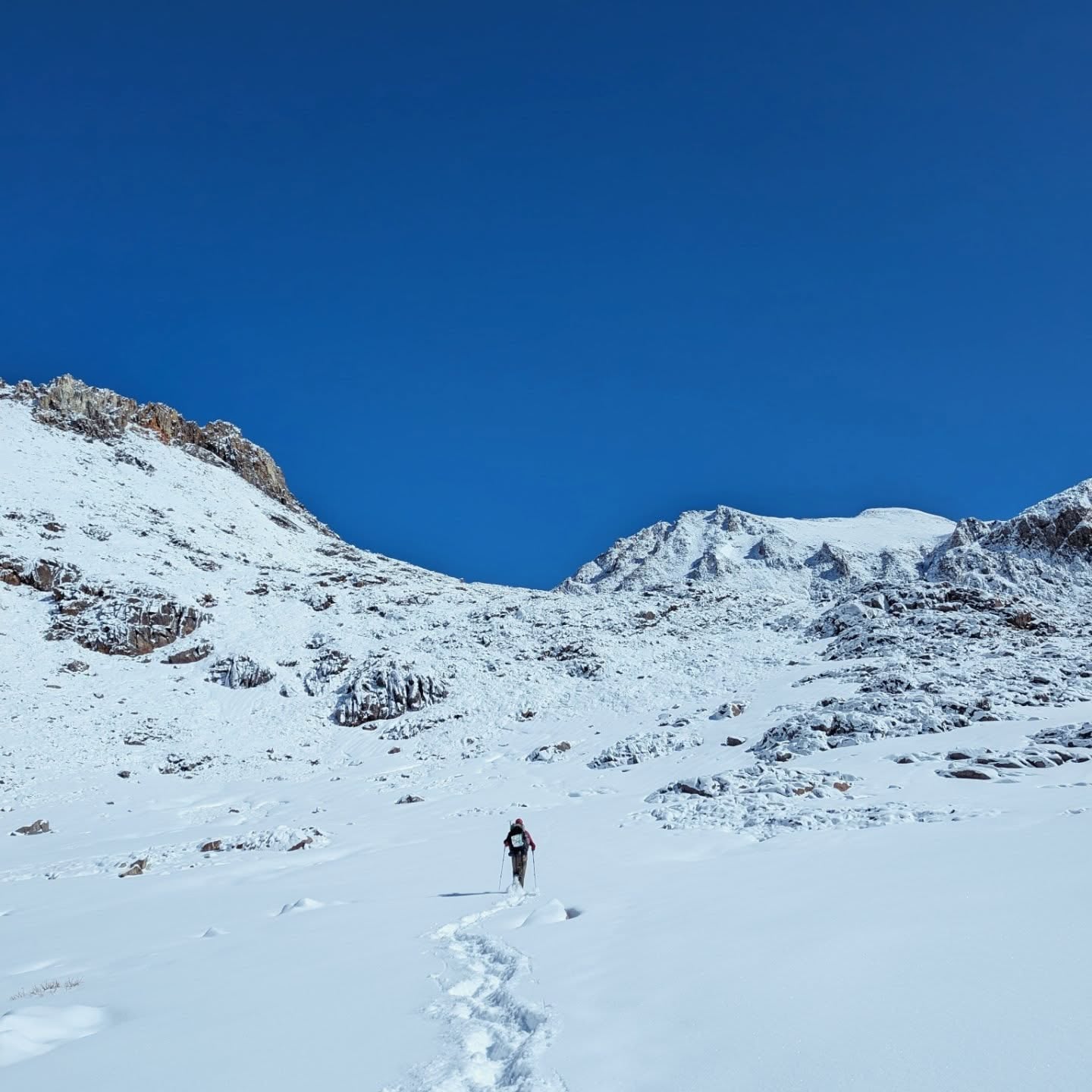 Randonneur au bout d’une trace de pas qui monte dans la neige entre des montagnes.
