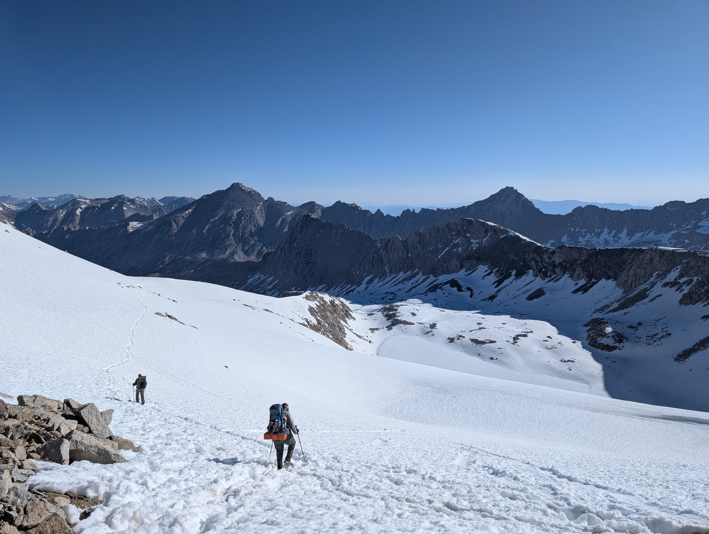 Deux randonneurs descendent dans la neige au milieu de hautes montagnes rocheuses.