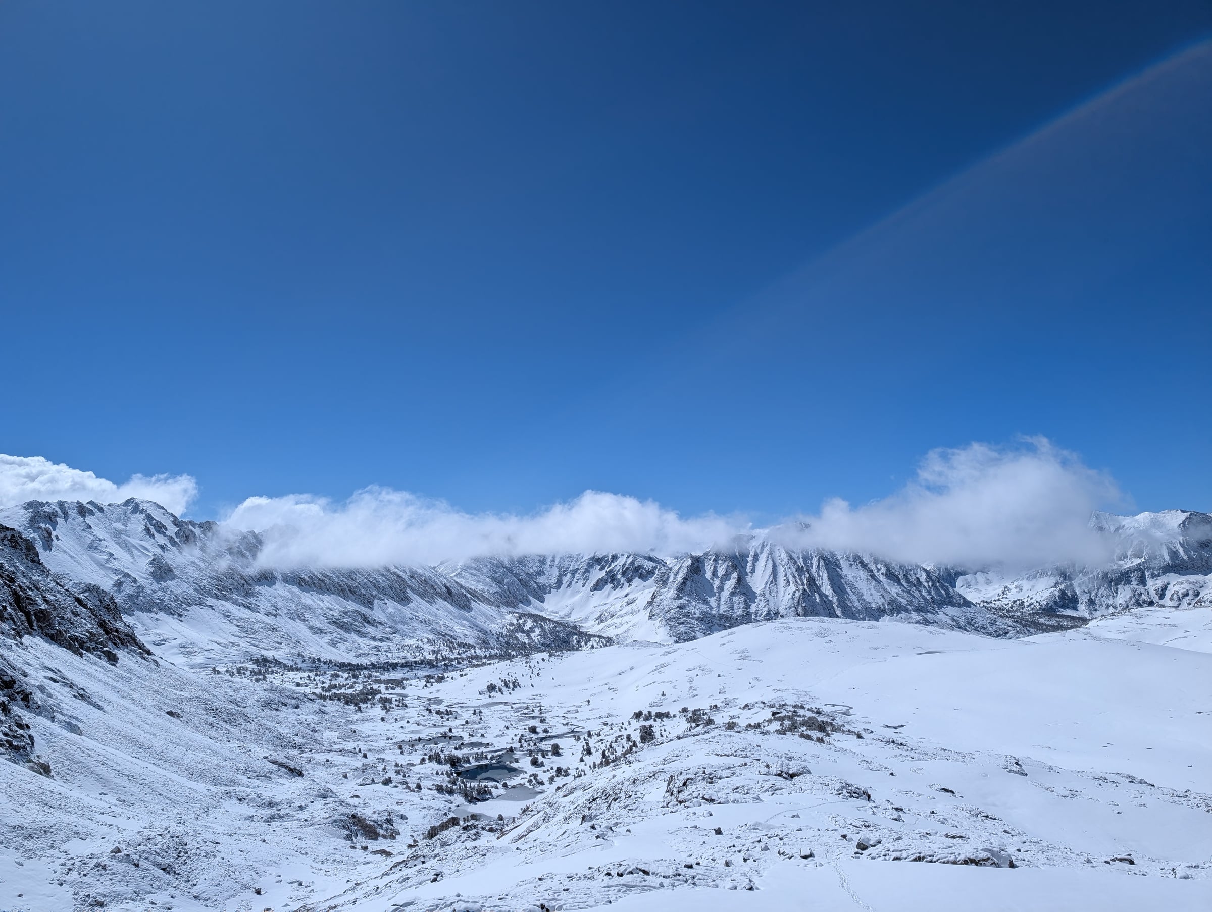 Vaste bassin de montagnes enneigées et de petits lacs sous un ciel bleu.