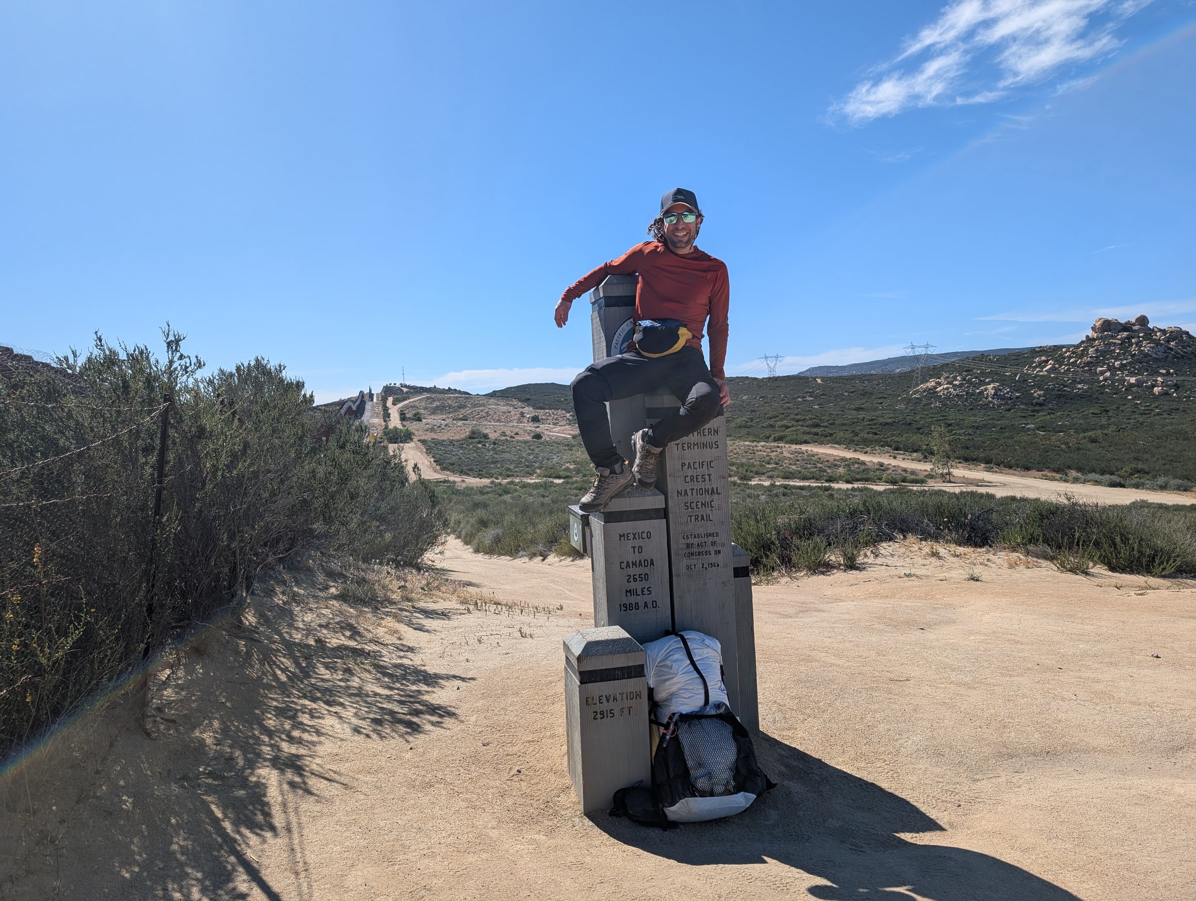 Randonneur assis sur le monument du terminus sud du Pacific Crest Trail, dans un paysage aride.
