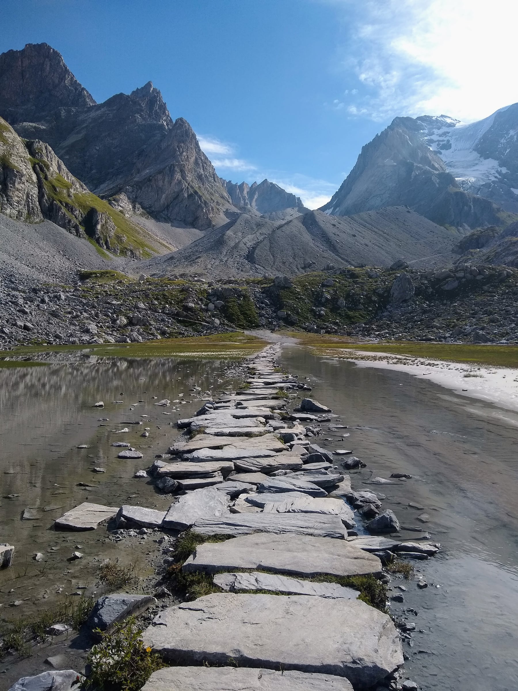 Chemin de pierres traversant l’eau d’un lac, face aux sommets rocheux de la Vanoise.