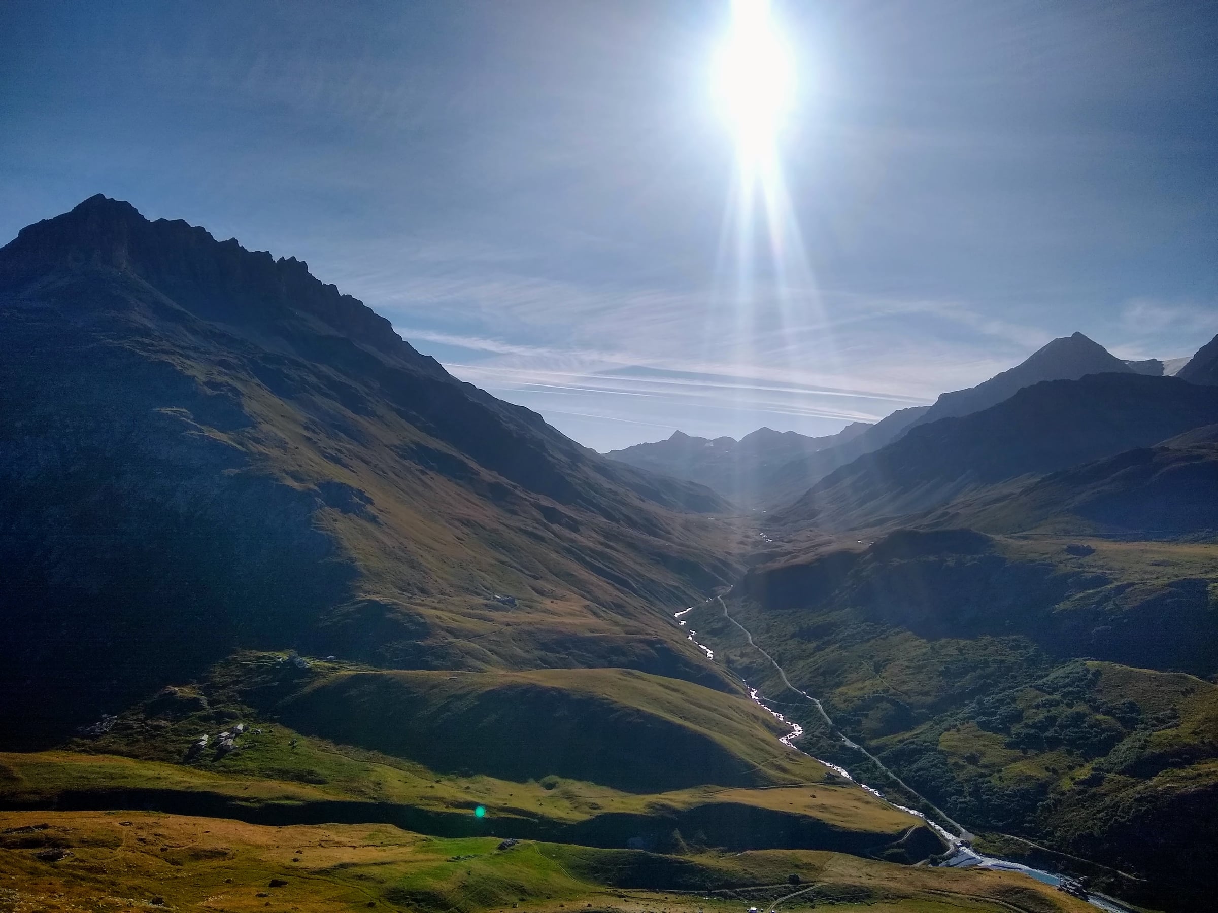 Soleil au-dessus d’une vallée alpine et d’un cours d’eau qui serpente entre les pentes.